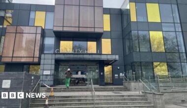 A modern-looking council building.  There are steps leading to the entrance which has sliding doors.  A person is leaving the building and walking towards the camera.