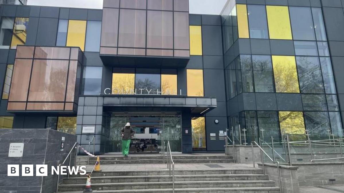 A modern-looking council building.  There are steps leading to the entrance which has sliding doors.  A person is leaving the building and walking towards the camera.