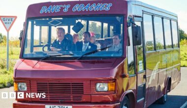 A still from Gavin and Stacey showing actor Steffan Rhodri driving the Dave's Coaches bus, with Rob Brydon, James Corden, Larry Lamb and Alison Steadman as passengers.