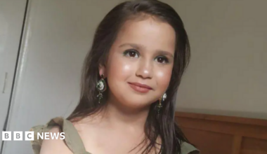 a little girl with long brown hair, wearing make-up and long dangly earrings