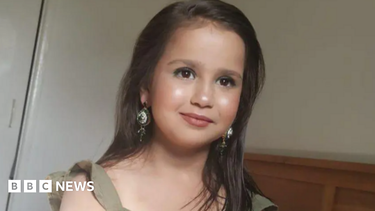 a little girl with long brown hair, wearing make-up and long dangly earrings