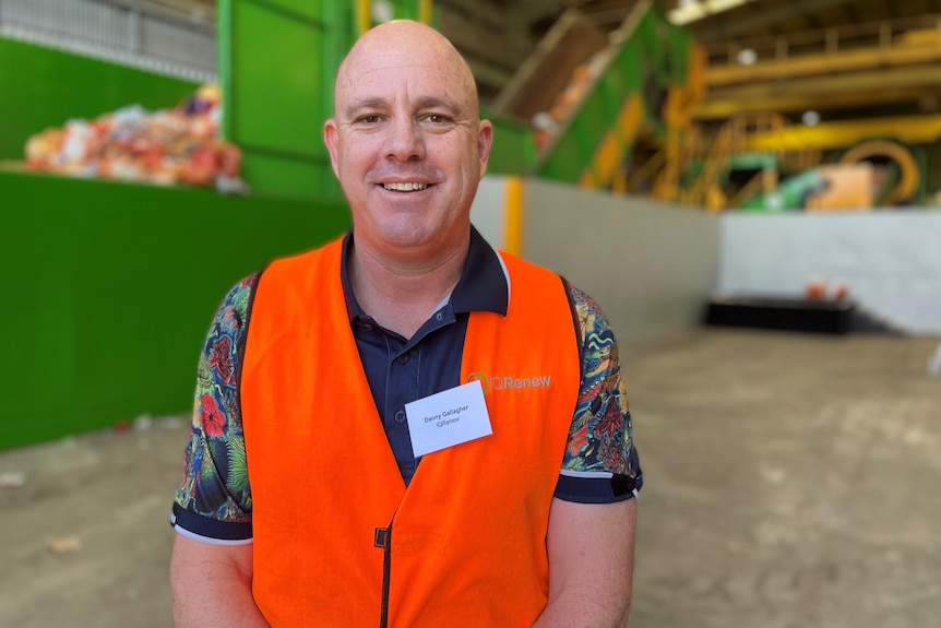 A man in an orange hi-vis vest stands in a warehouse in front of a large green machine.