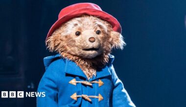Paddington on stage in the West End, wearing his trademark blue coat and red hat