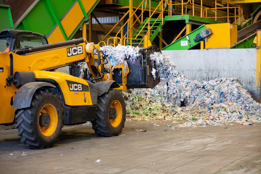 Machinery moves piles of household soft plastic waste at a recycling facility.