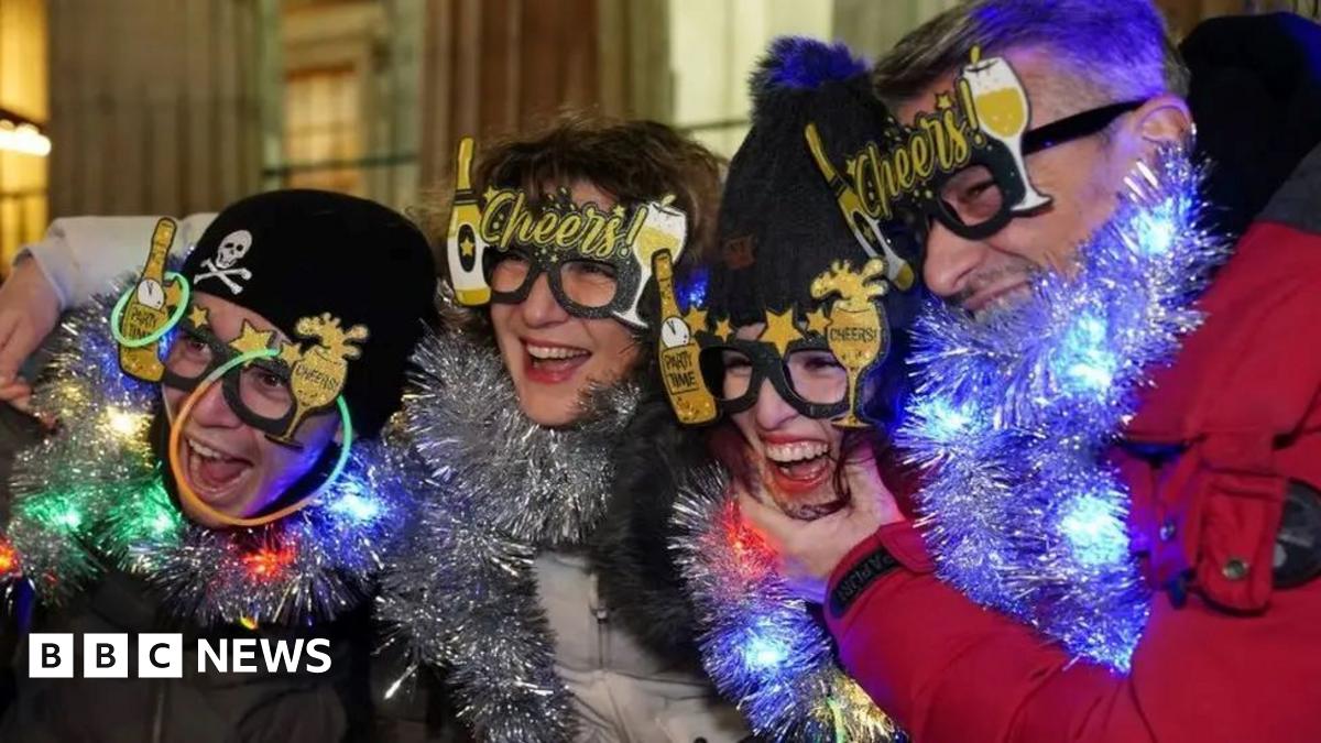 Four revellers wearing funny glasses and tinsel. They are all laughing. Two are wearing dark woolly hats.