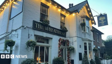 The outside of the Wheatsheaf pub - a white brick building with a pitched black roof. There are Christmas lights lining the roof.