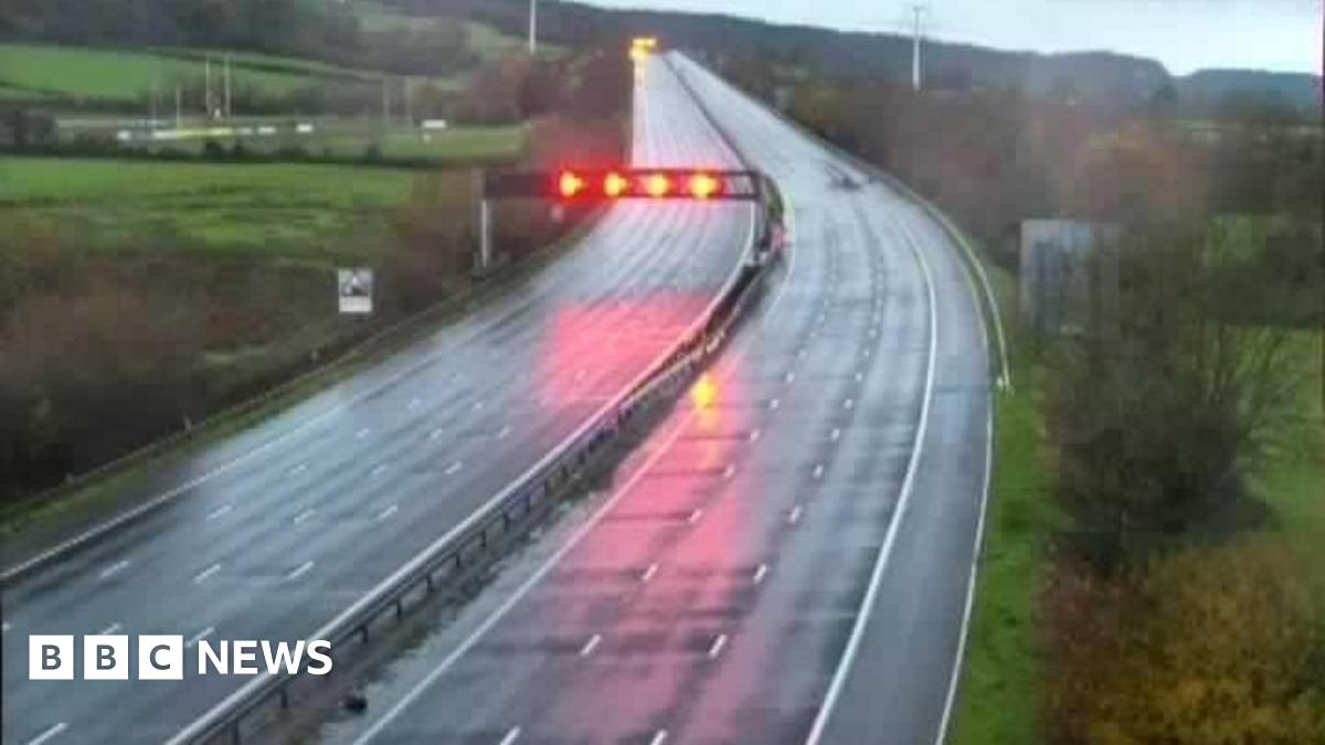 An empty motorway at the dawn with car lights and rain. Image from a motorway camera.