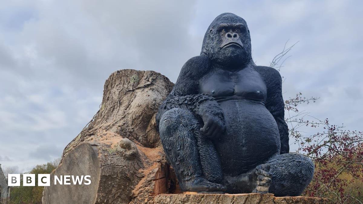 A large gorilla statue sitting on a tree stump as viewed from below.