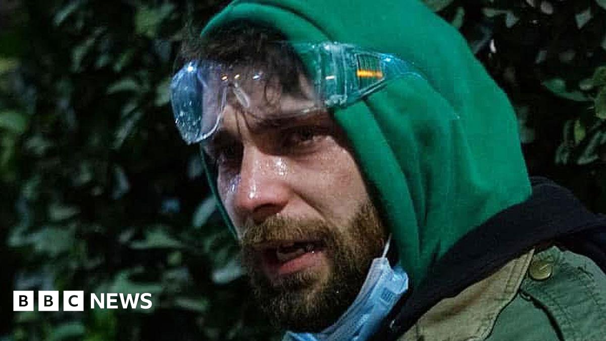 Crowds scatter as water is sprayed out from trucks in the Georgian capital - there is a large plume of water and widely dispersed mist. It is dark and the shot is taken from above.