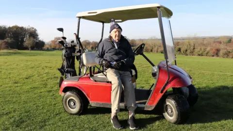 Archie is pictured sat on a red golf buggy with a bag of golf clubs on the back
