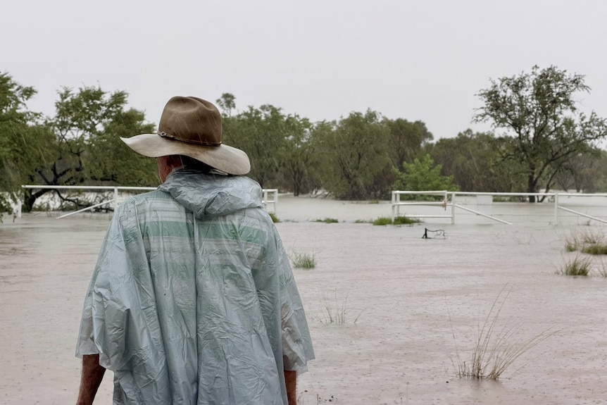 A person in a raincoat looks at a flooded property.