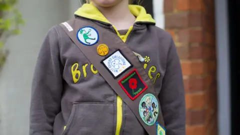 Alamy A girl wearing a brownies hoody and a sash with badges on 