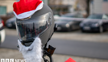 A helmet is placed on a motorbike's handlebars, dressed with a santa hat and beard.