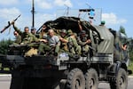 Pro-Russian militants sitting atop a truck drive past a checkpoint in Makiivka