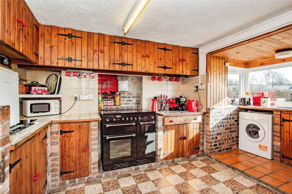 Rustic kitchen with wood cabinets, tiled countertops, double oven and exposed brick walls.
