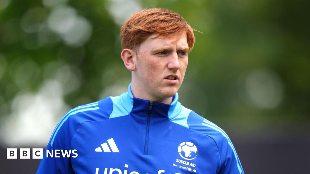 Angry Ginge wear a blue soccer aid half zip top which has lighter blue markings on the neck