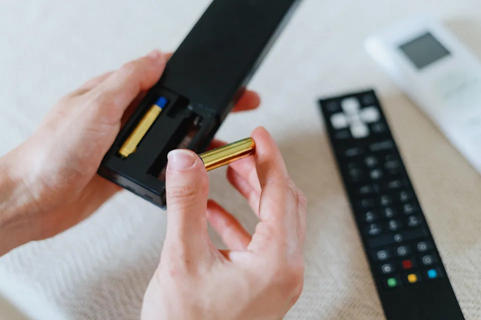 Hands insert a battery into a remote control, highlighting a task related to managing household electronics