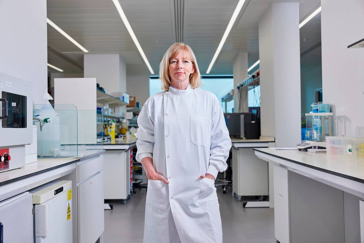 An individual dressed in a white lab coat is standing in a modern laboratory, with various scientific instruments and equipment visible in the background.