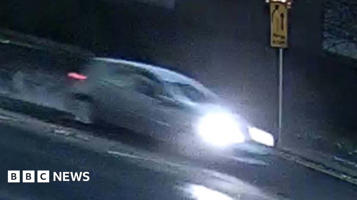 A blurred picture of a car, with its headlights on, driving down a road.