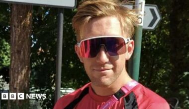 A smiling man wearing sunglasses and a red top.