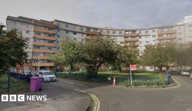 A block of curved flats which are mainly white with orange balconies.