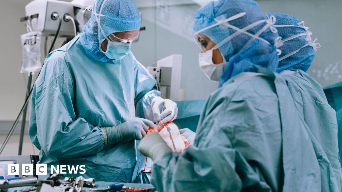 A group of doctors wearing blue scrubs, masks and hairnets. They are in a surgical theatre performing a knee replacement operation on a patient.