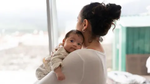 Getty Images A mother holds her baby upright to rest on her shoulder