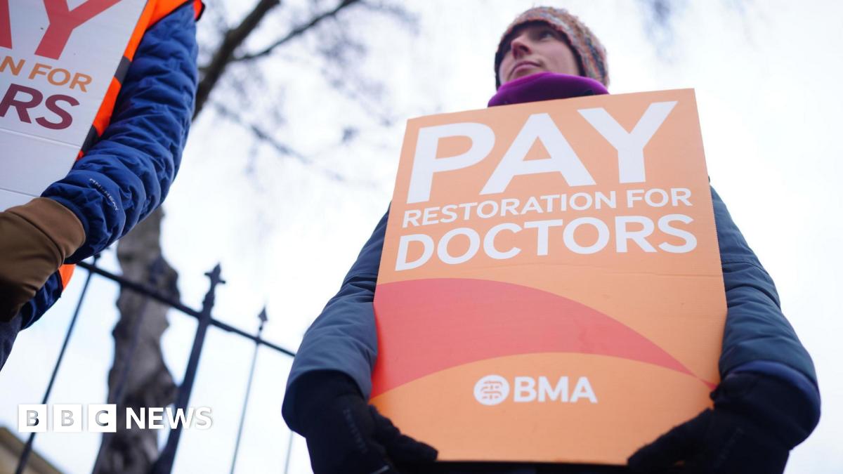 Doctors dressed in outdoor winter clothes hold strike posters - one says, "Pay restoration for doctors"