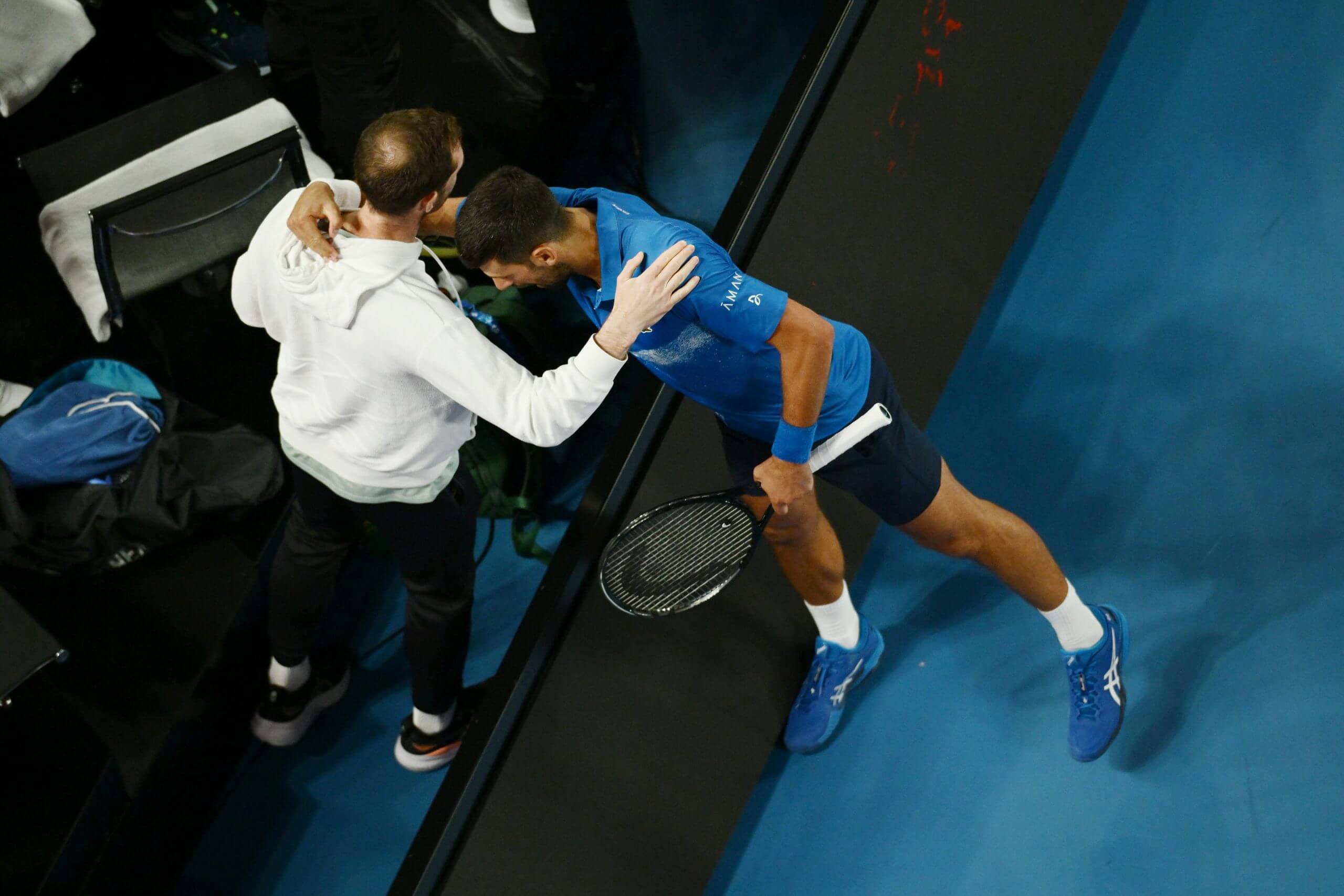 Andy Murray stands as Novak Djokovic embraces him across a barrier on Rod Laver Arena in Melbourne.