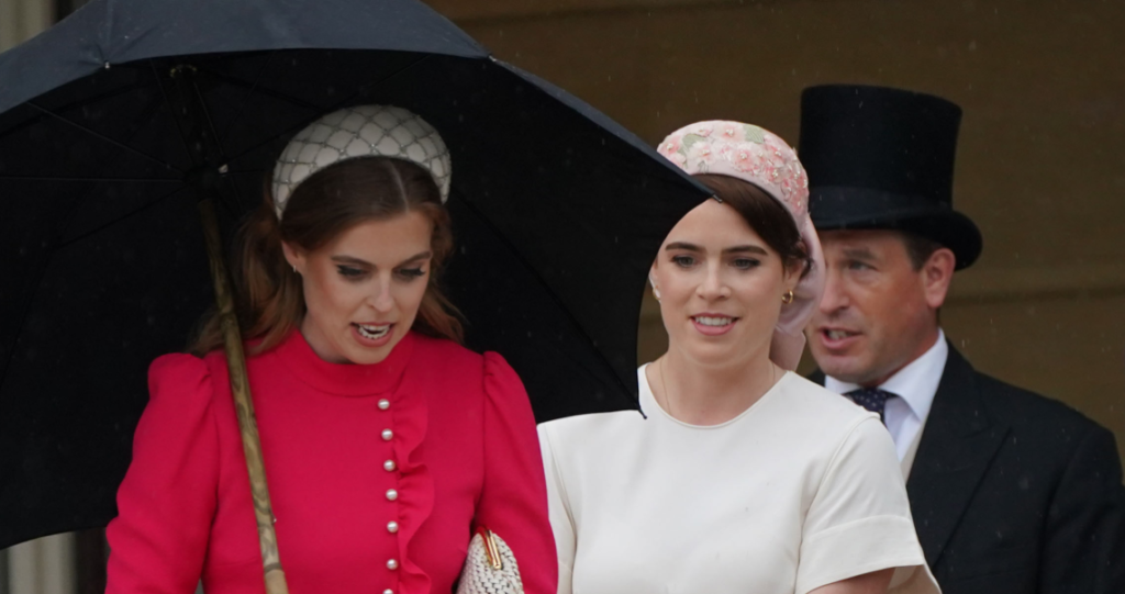 Princess Beatrice and Princess Eugenie wearing pink dresses walk down the steps into the garden of Buckingham Palace
