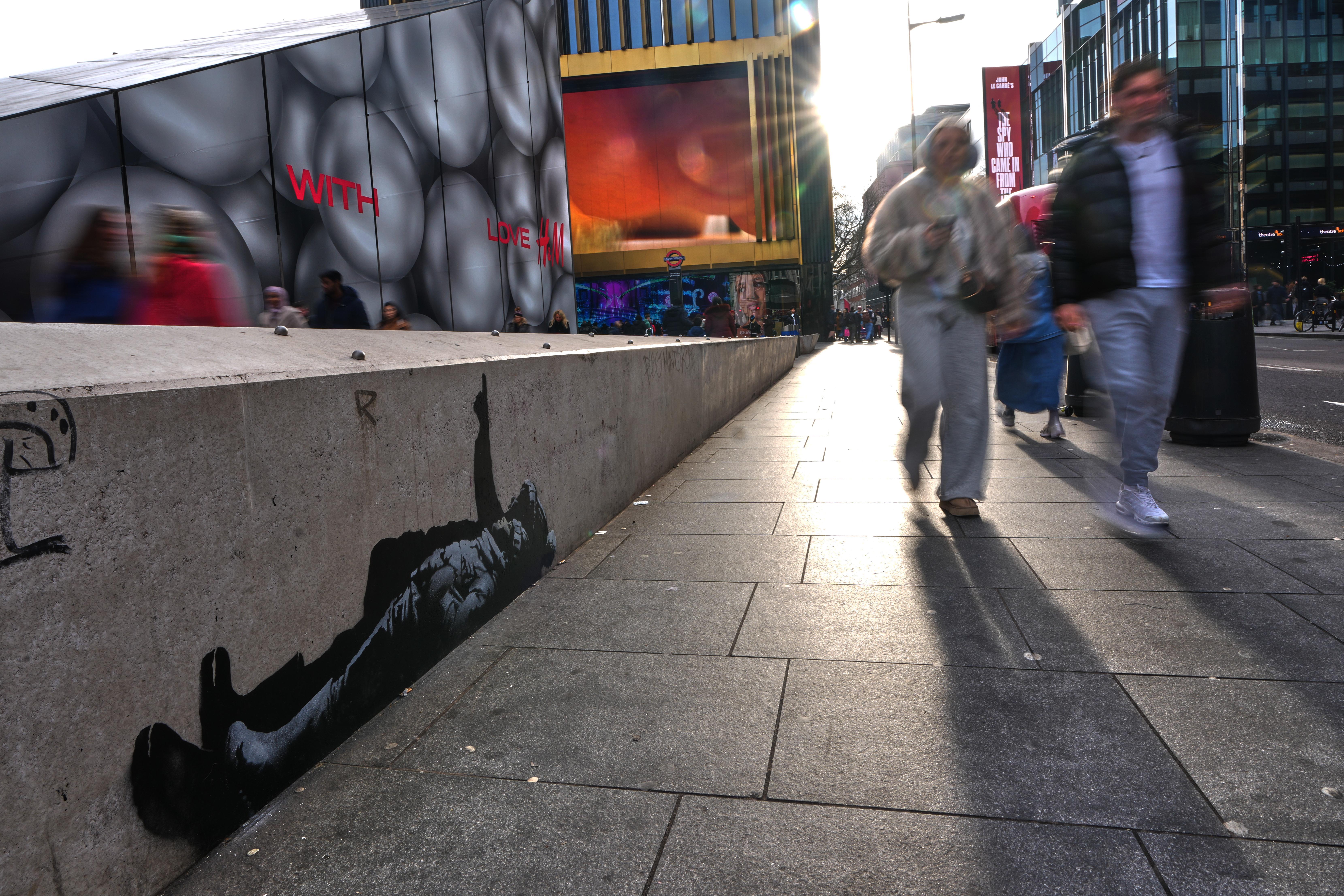 Pedestrians walk past a graffiti artwork, depicting two people, which...