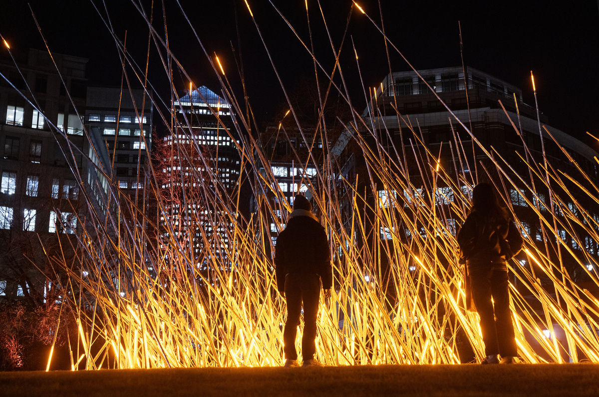 someone stood in front of a flickering light installation at night that resembles a fire burning