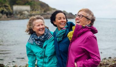 Friends and sisters exploring the outdoors together in Cornwall. They are standing with their arms around each other at the coast.