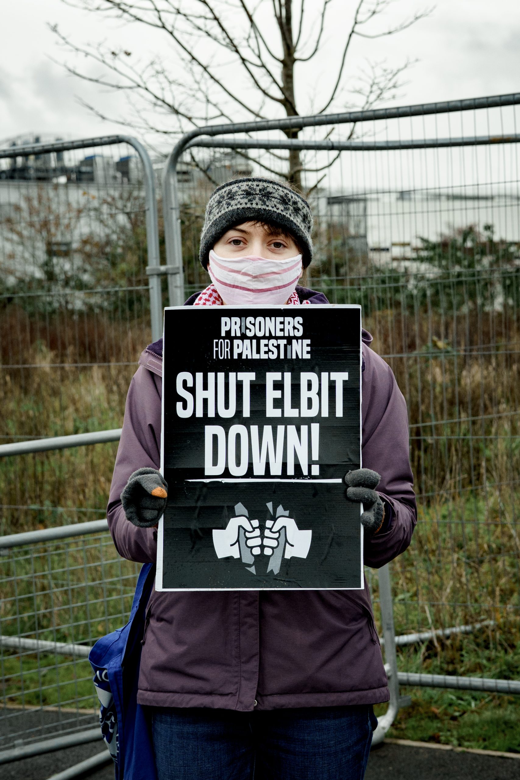 A young woman in a purple jacket holds a placard. 