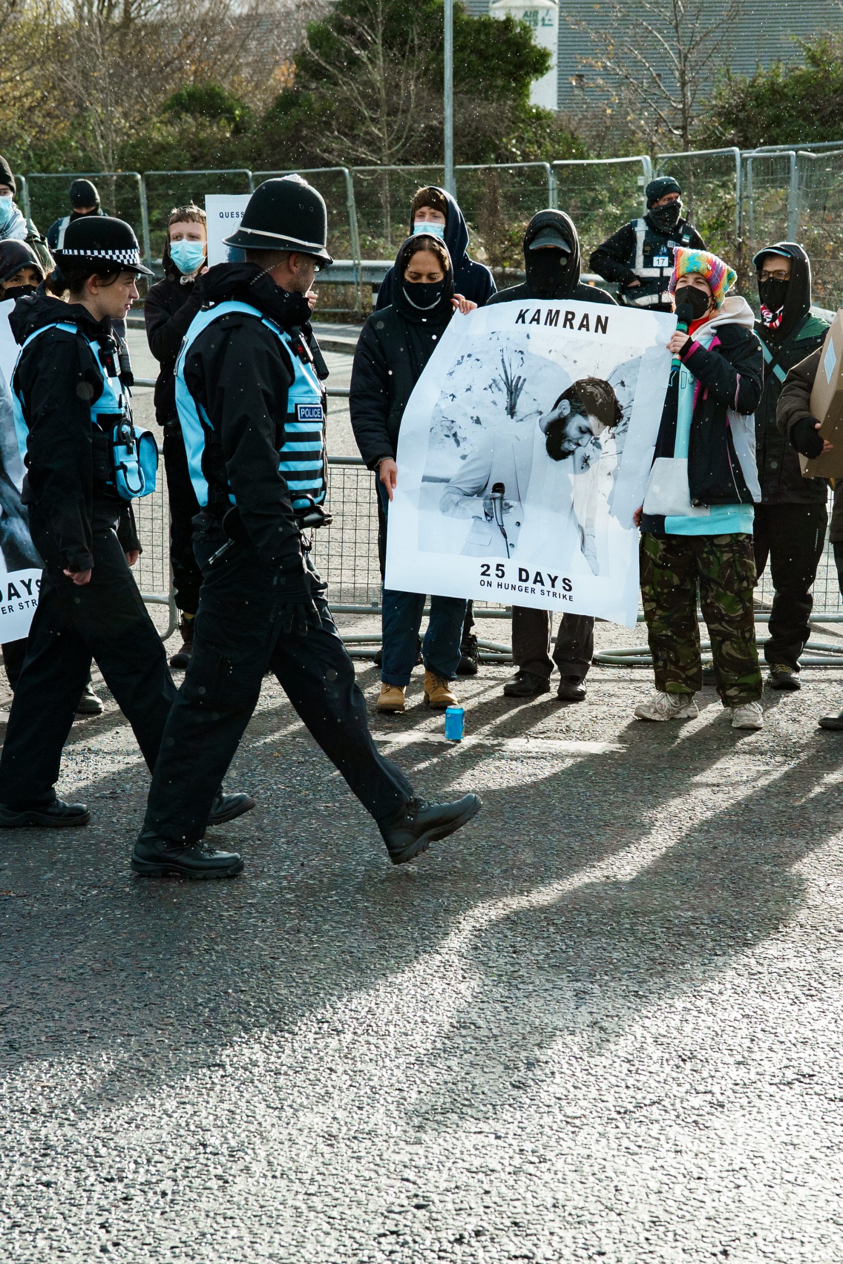 Police officers walk past protesters holding banners on a road. 