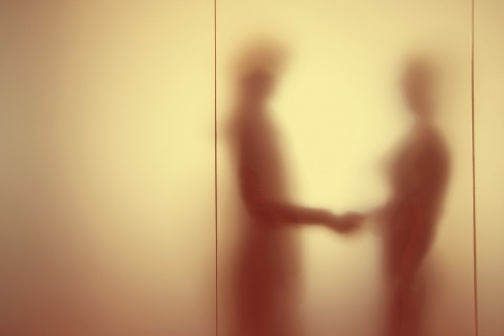 A blurred image of two people shaking hands behind a wall