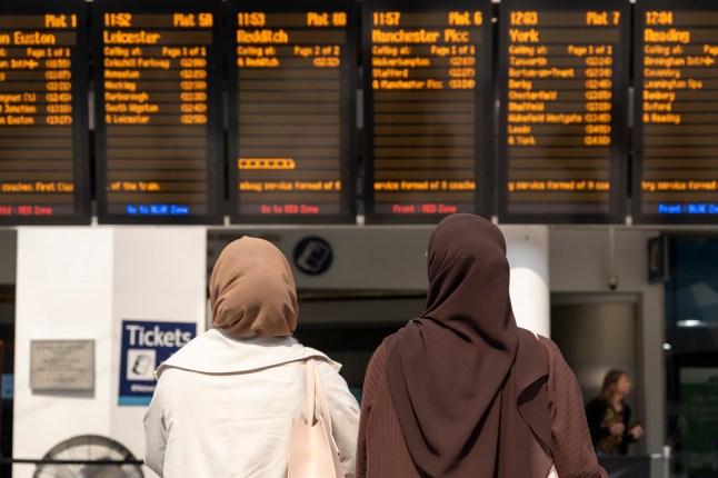 Two women looking at a train departure station board.