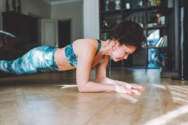 woman in sportswear do plank exercise at home on a floor of living room