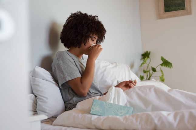 Young woman with a cold checking her temperature in bed.