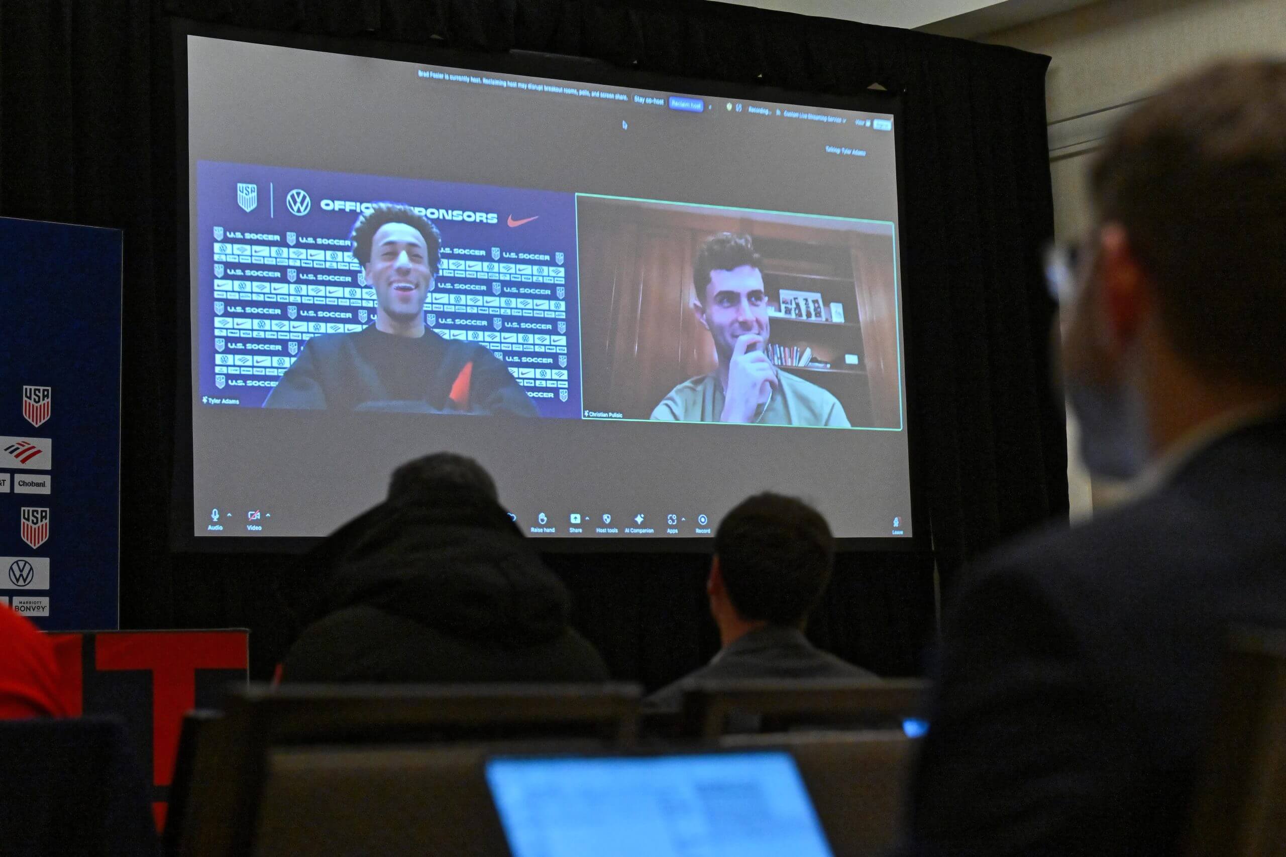 Tyler Adams, left, and Christian Pulisic, right, are on a screen as they speak remotely to a room full of media.