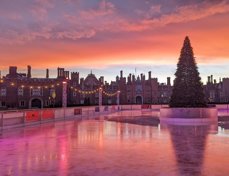 the stunning Hampton Court Palace Ice Rink in front of hampton court palace, with a christmas tree in the middle of it, lit by stunning dusk lighting