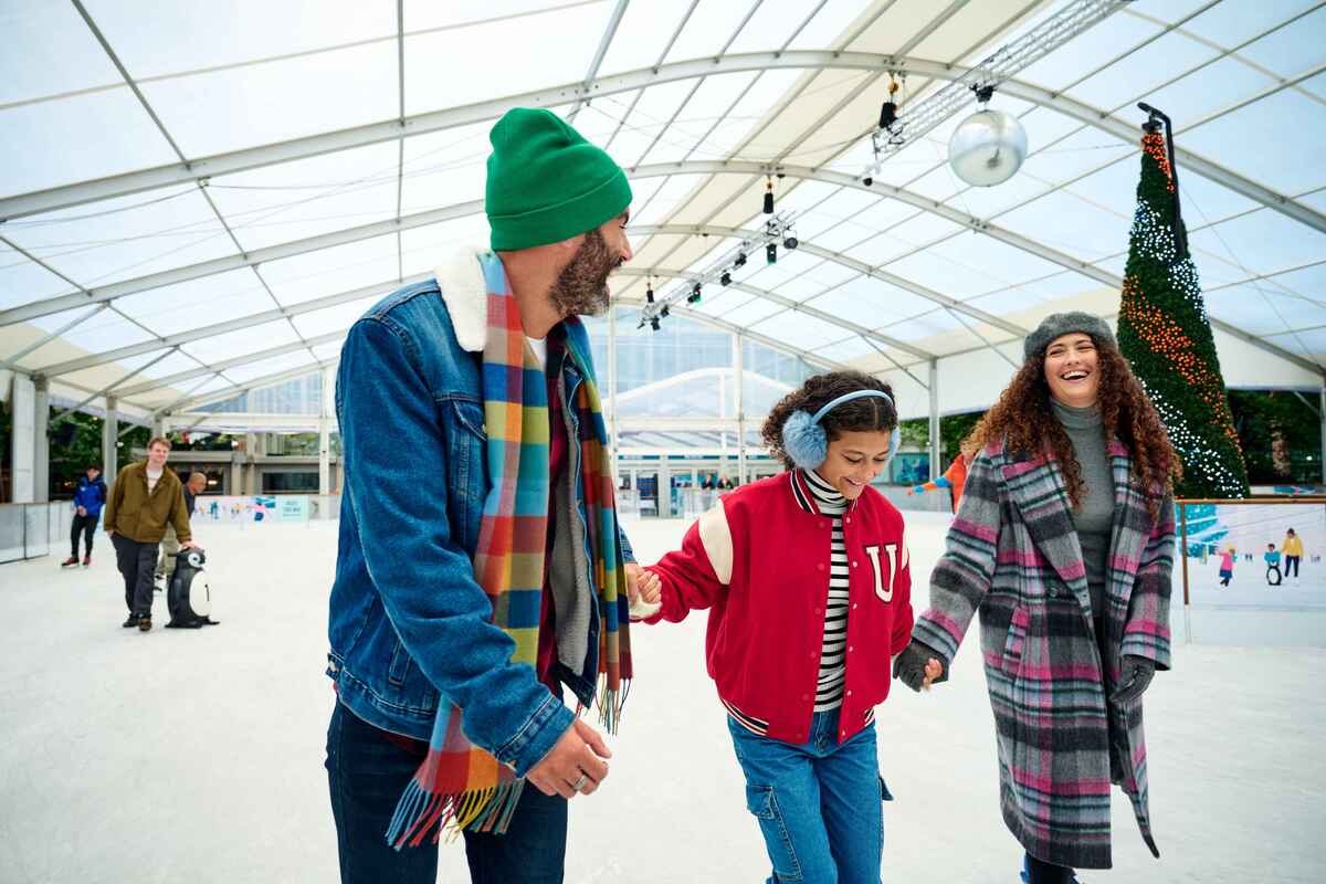 three people holding hands and enjoying a skating session at ice rink canary wharf