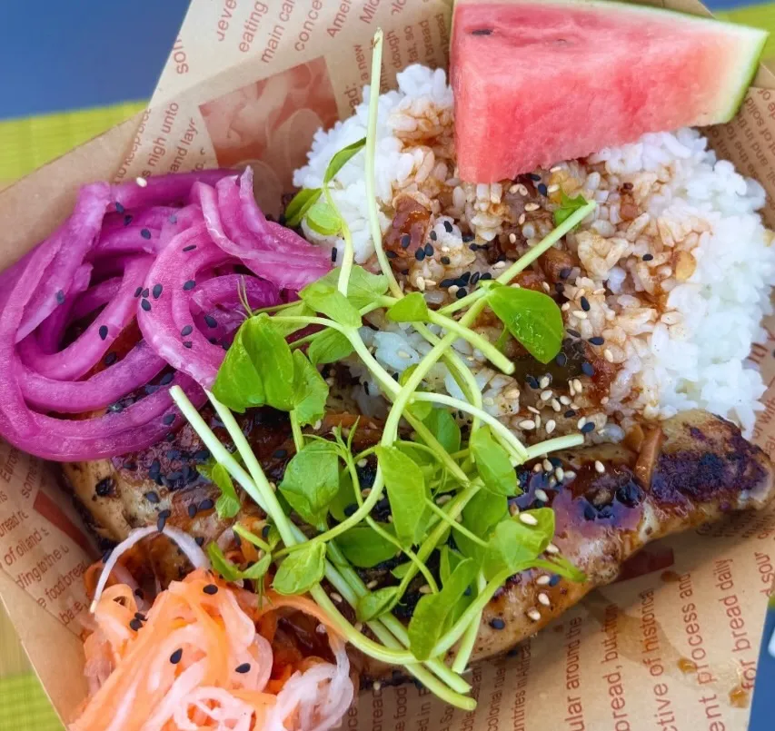 Grilled chicken with white rice, pickled red onions, microgreens, and a slice of watermelon.
