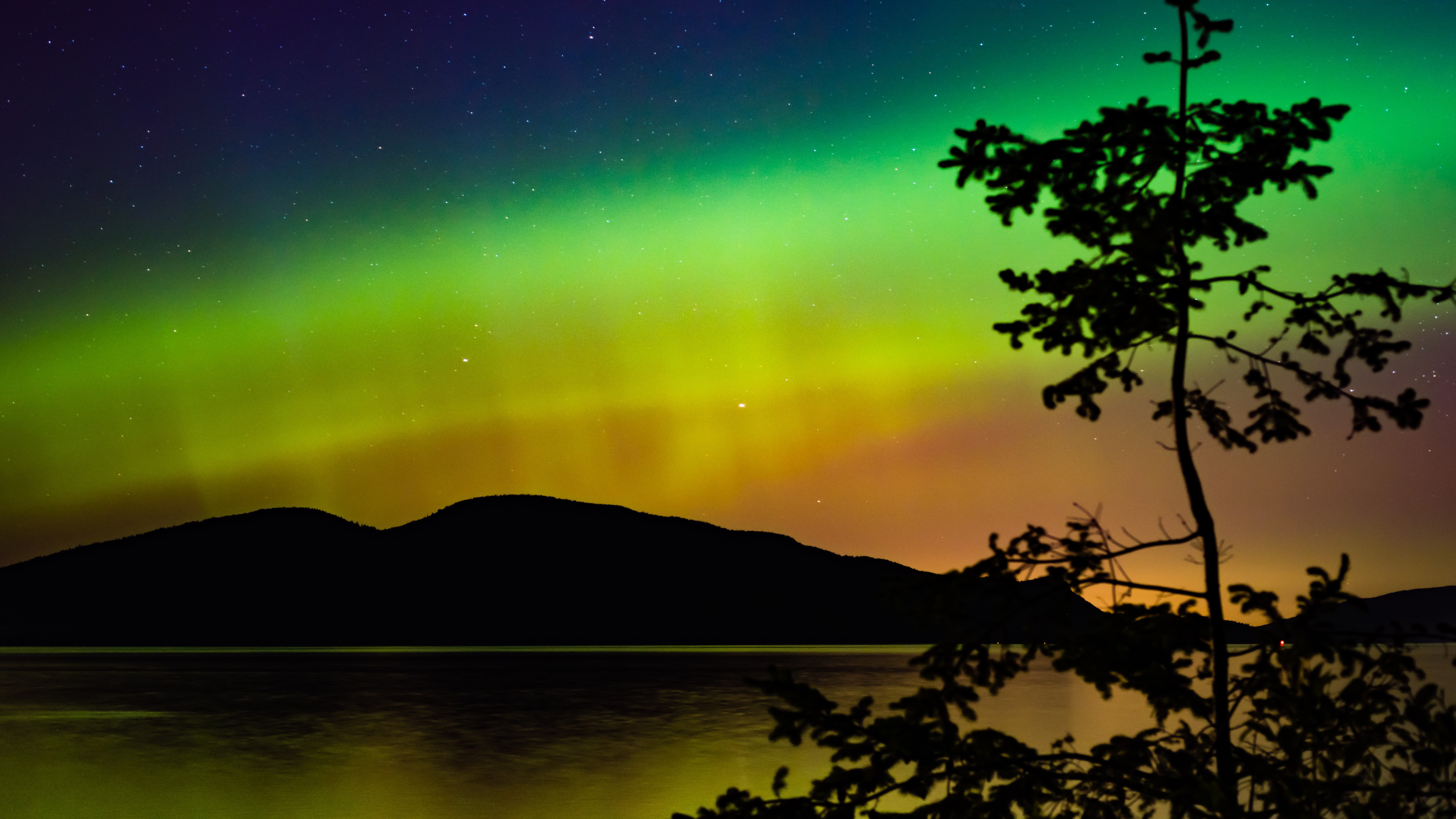 A photograph of green and orange auroras above Cypress Island in the U.S.