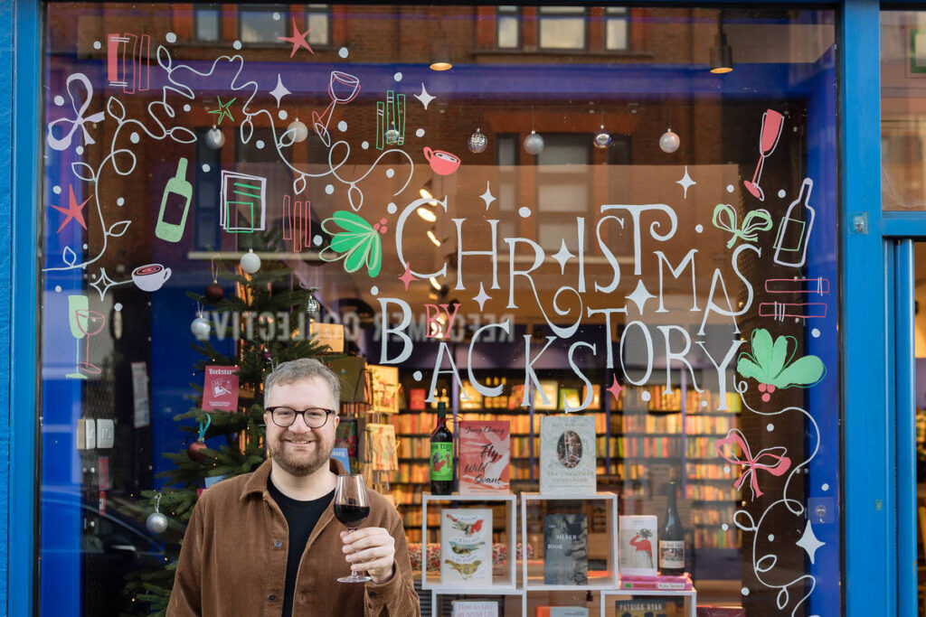 Tom Rowley at Backstory bookshop holding a glass of wine