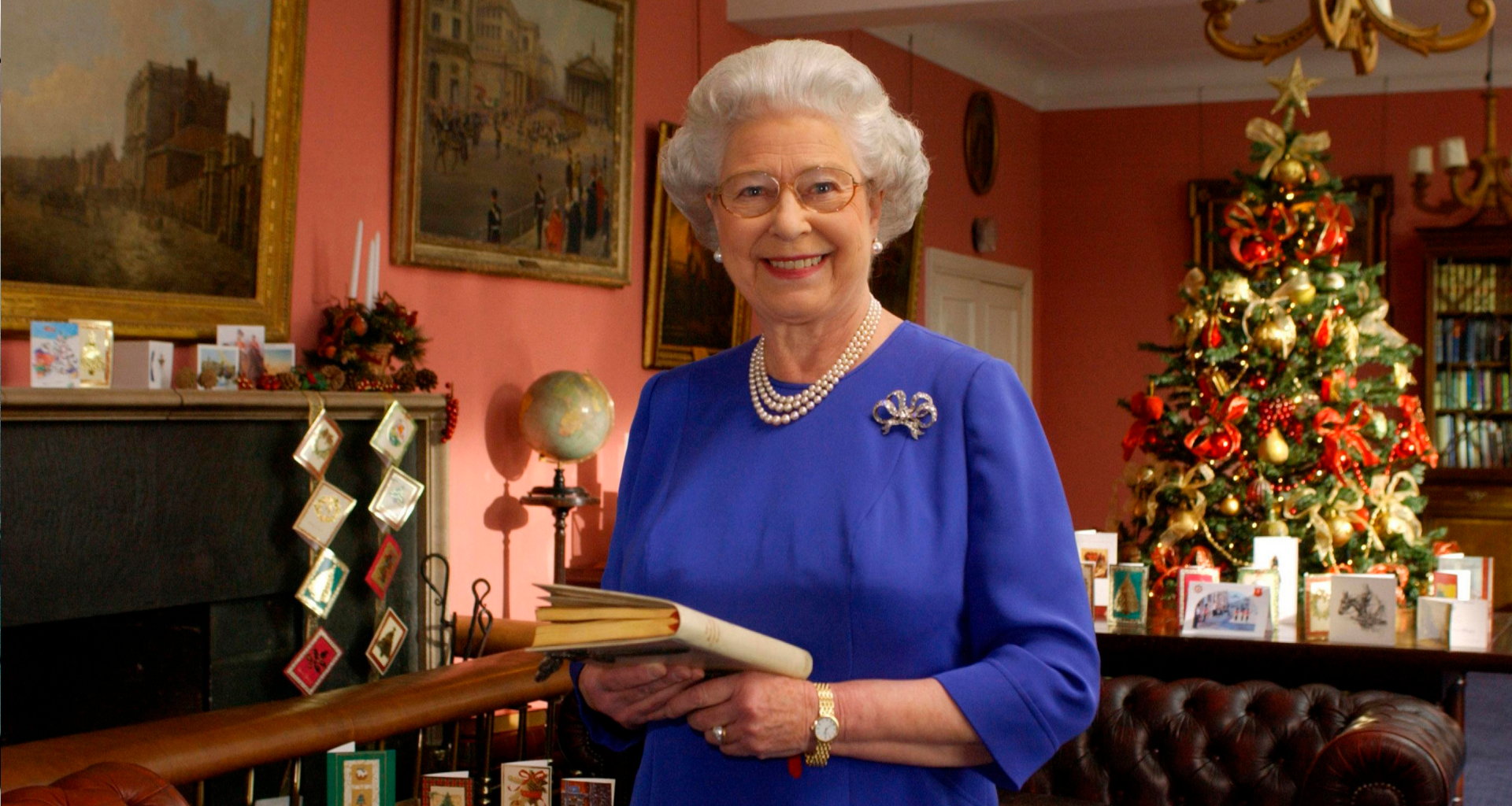 Queen Elizabeth wearing a blue dress standing in front of a Christmas tree