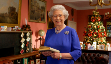 Queen Elizabeth wearing a blue dress standing in front of a Christmas tree