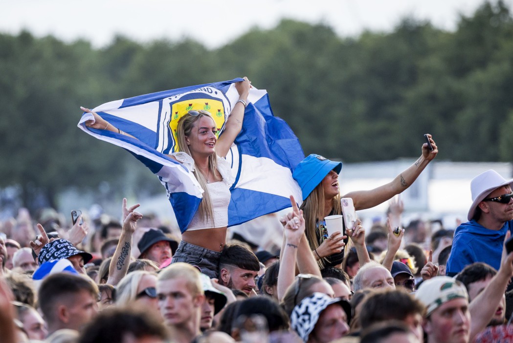 Two young women at a concert, one on shoulders holding a Scottish flag.
