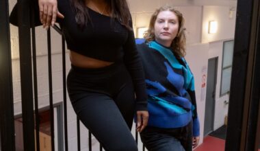 Two women lean against metal banisters in a stairwell