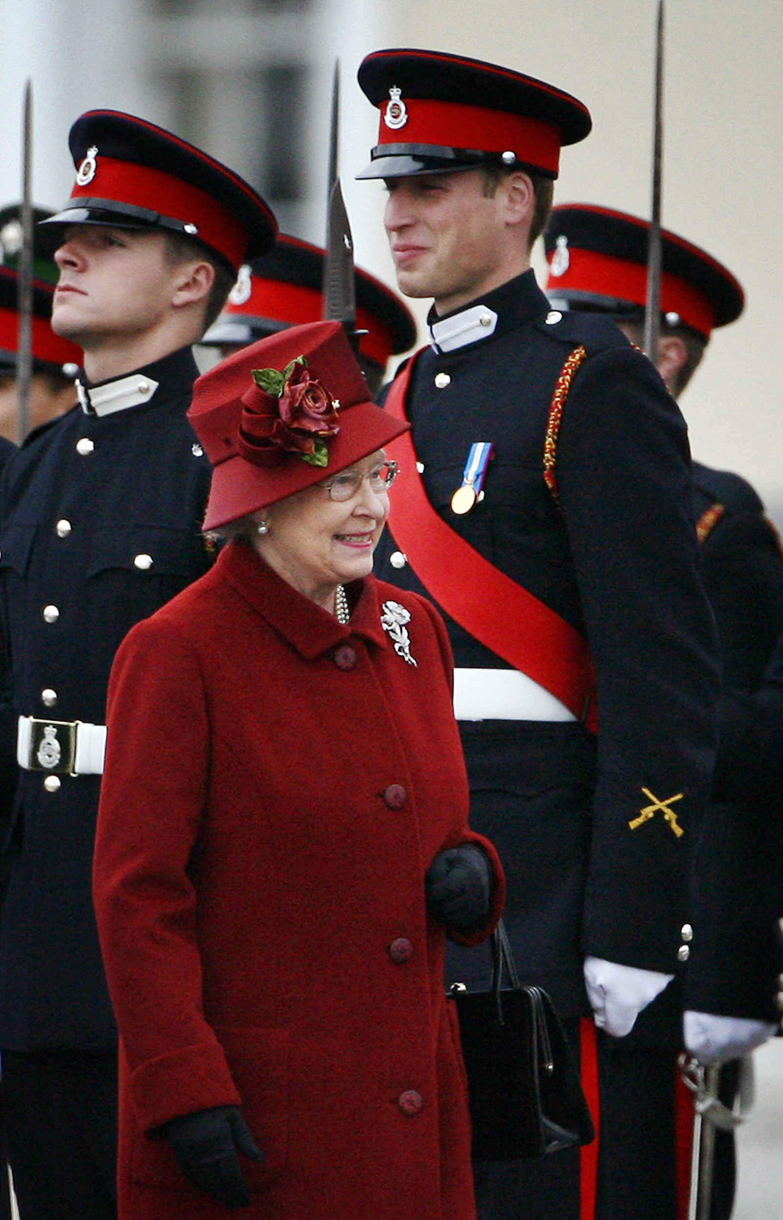 Queen Elizabeth wearing a red coat standing in front of Prince William at his Sandhurst graduation